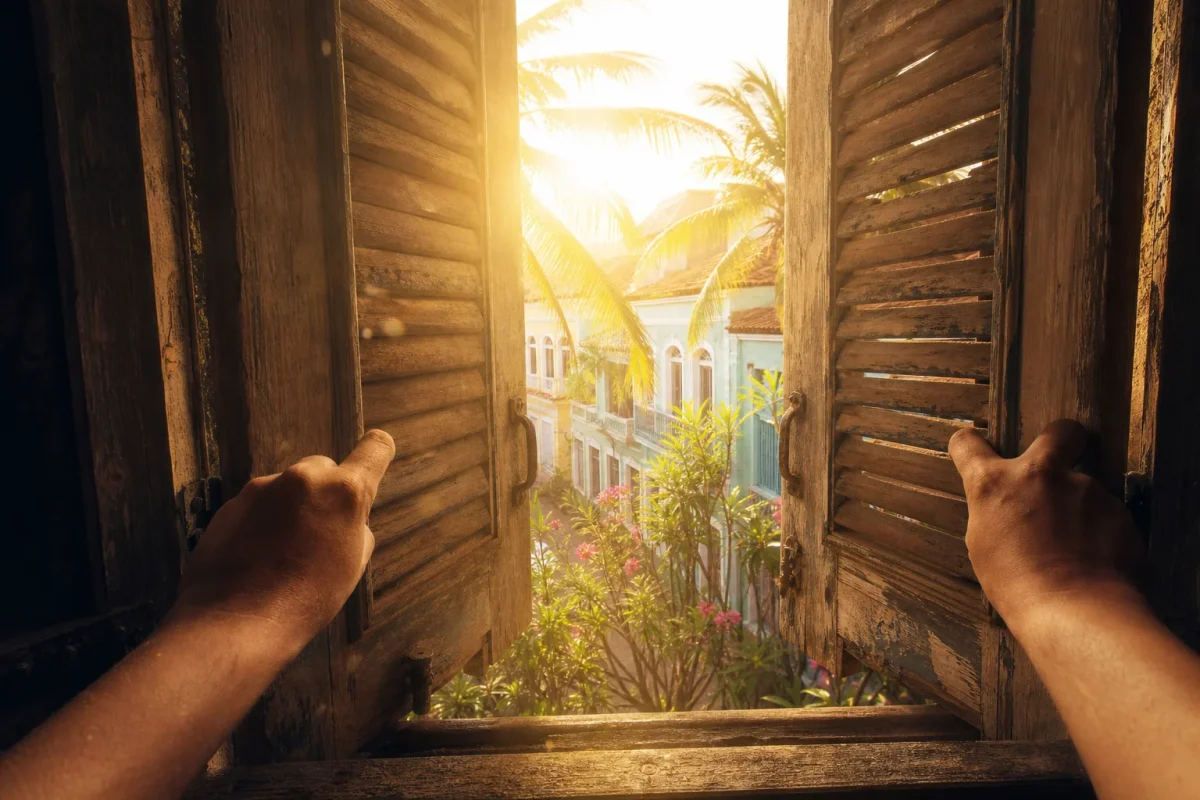 Manos abriendo las persianas de una ventana dejando entrar la luz de la mañana